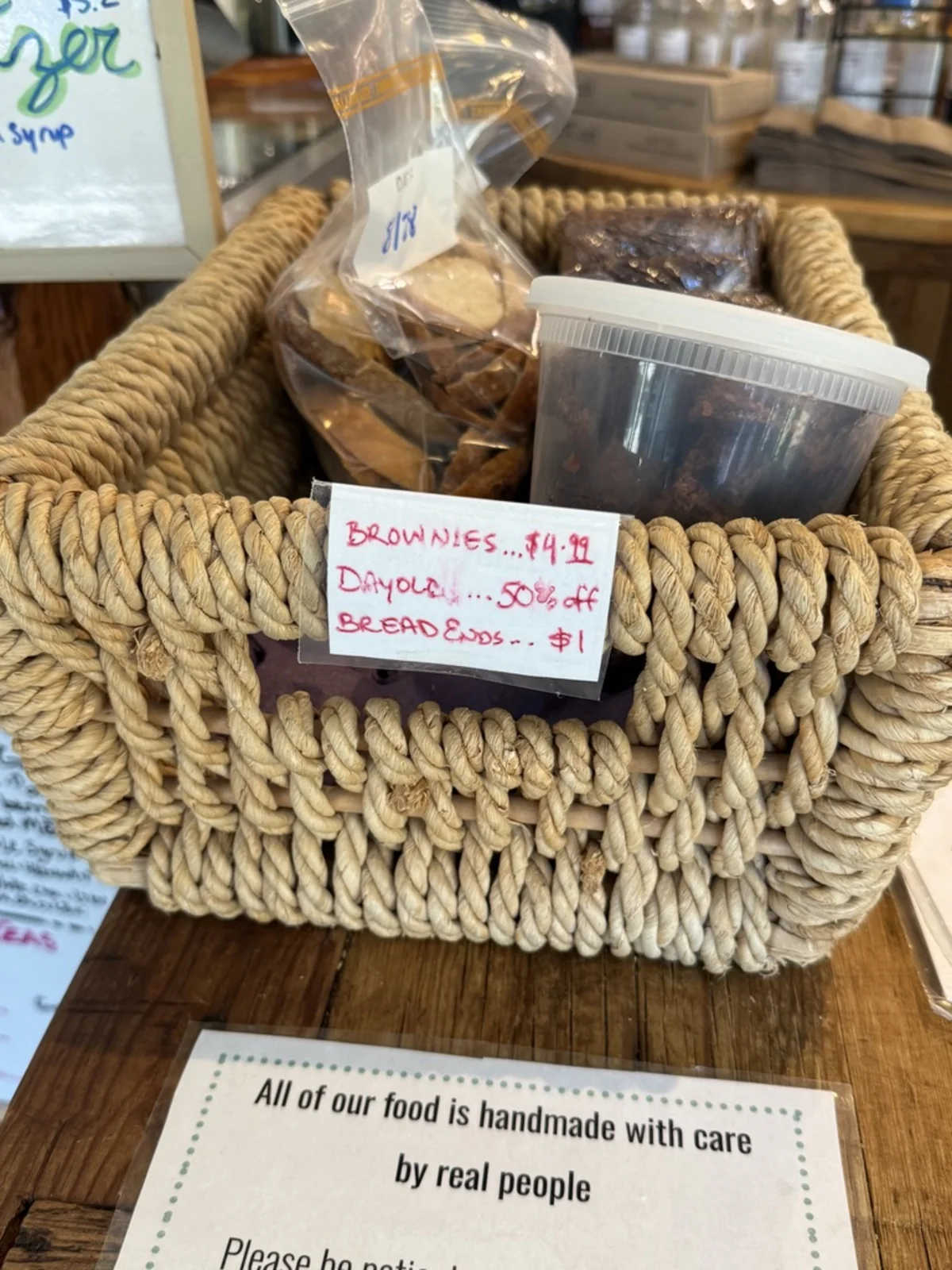 A rope basket of baked goods with a handwritten card: brownies $4.99, day old 50 percent off, bread ends $1.