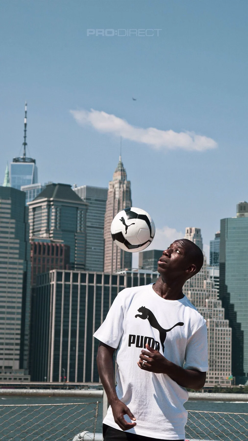 Bradley Wright-Phillips in a white Puma shirt heading a ball with the lower Manhattan skyline behind him.