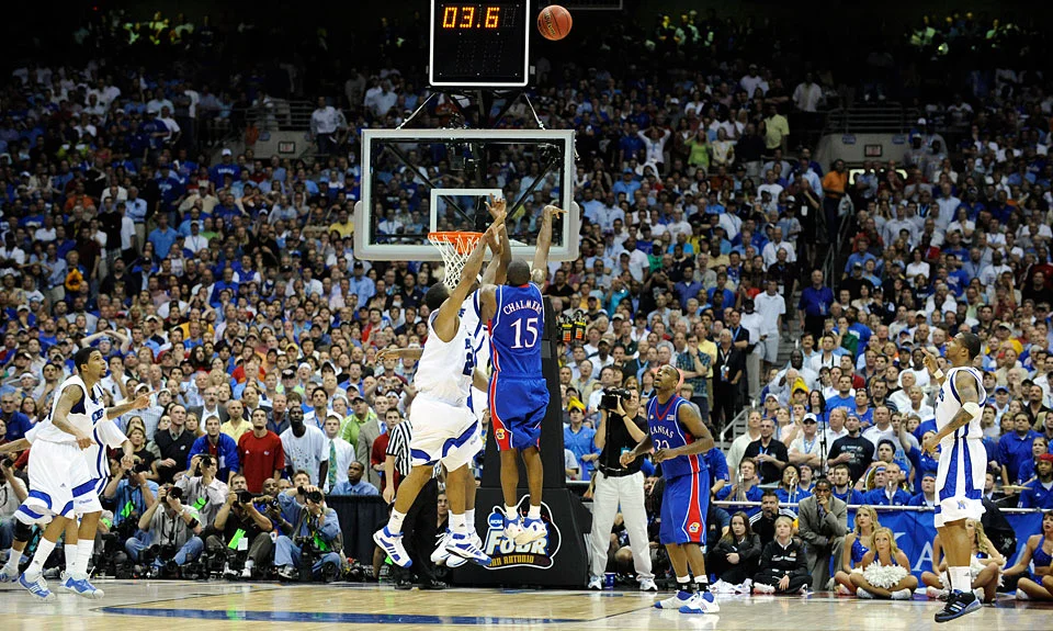 Mario Chalmers releasing a three-point shot with 3.6 seconds on the game clock in the 2008 NCAA basketball championship, viewed from behind the basket.