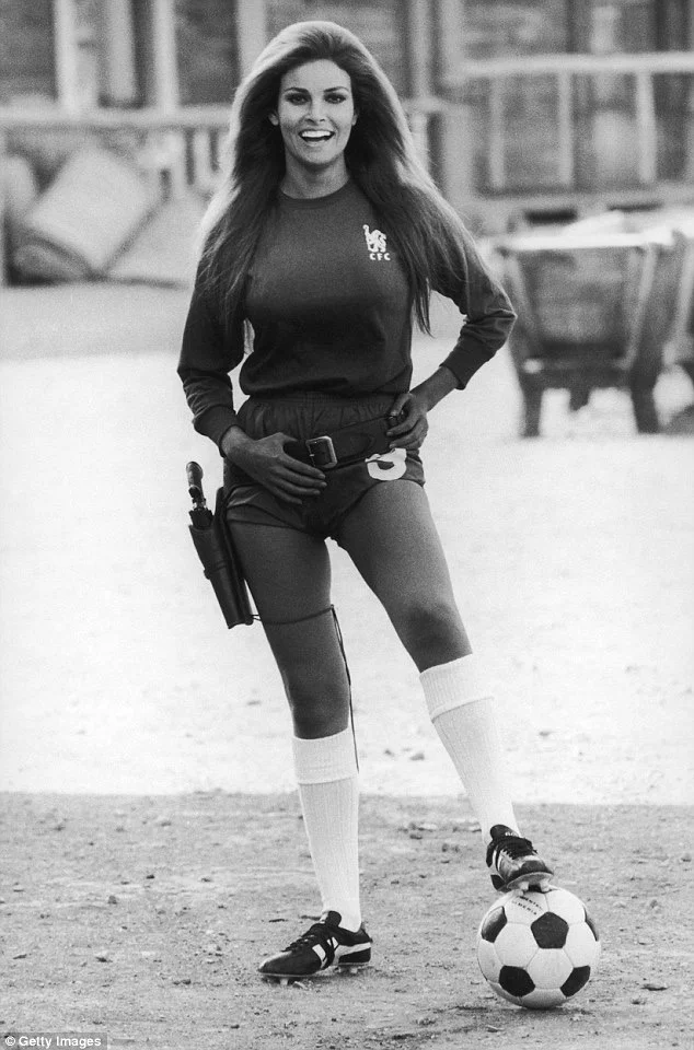 Raquel Welch on a dirt field wearing a Chelsea Football Club #9 jersey and shorts, standing next to a soccer ball.
