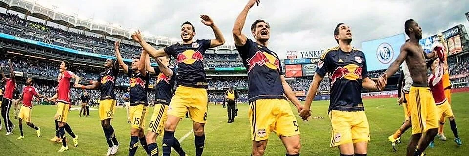 New York Red Bulls players holding hands and celebrating in front of the crowd at Yankee Stadium after a match.
